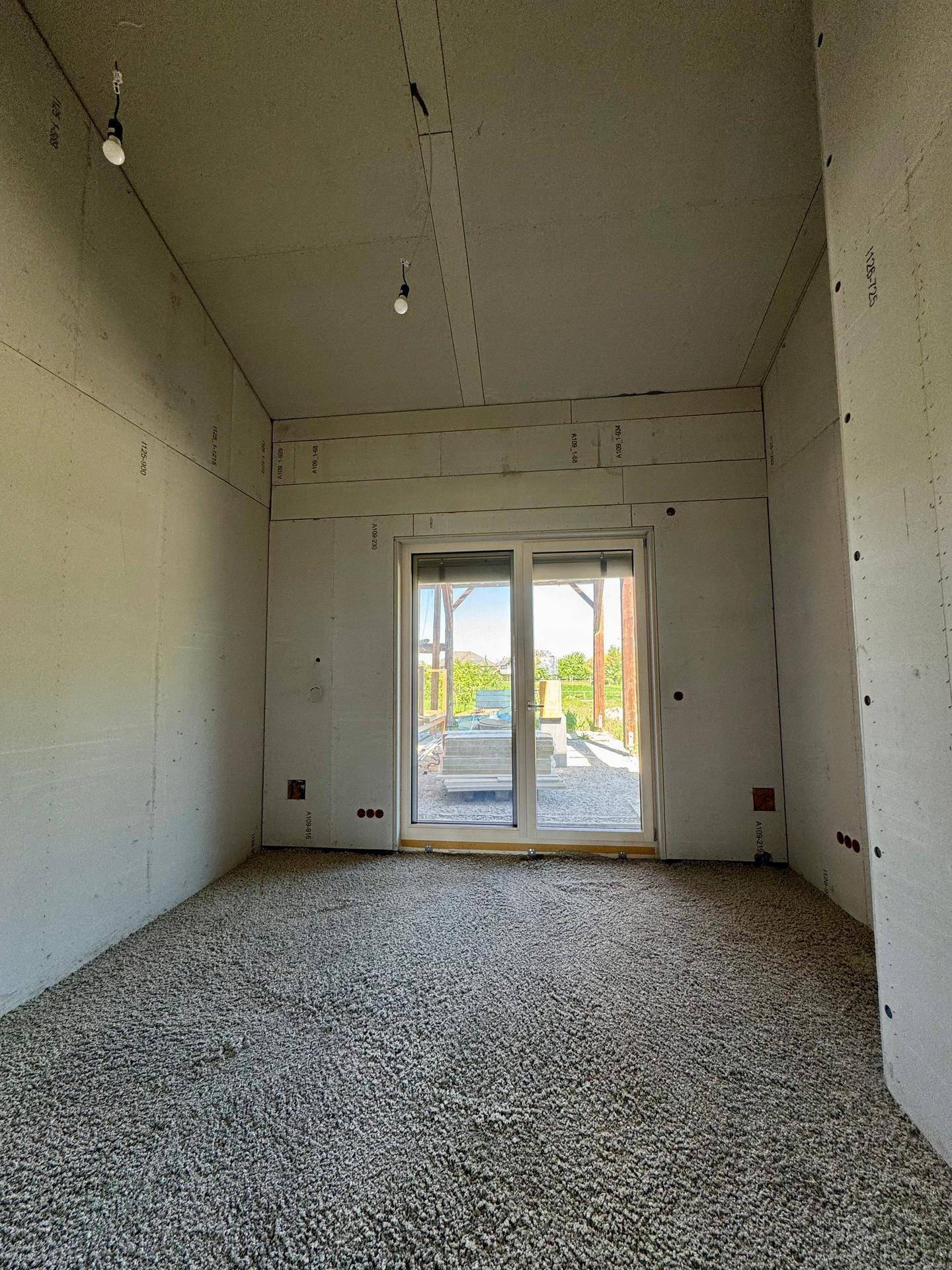 Helles Zimmer im Rohbau mit großer Schiebetür, die zu einem zukünftigen Außenbereich führt.