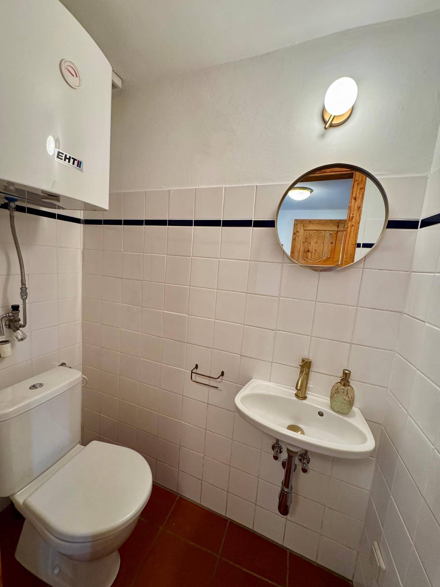 Separate Toilette mit Waschbecken, Spiegel und weiß-blauen Fliesen.