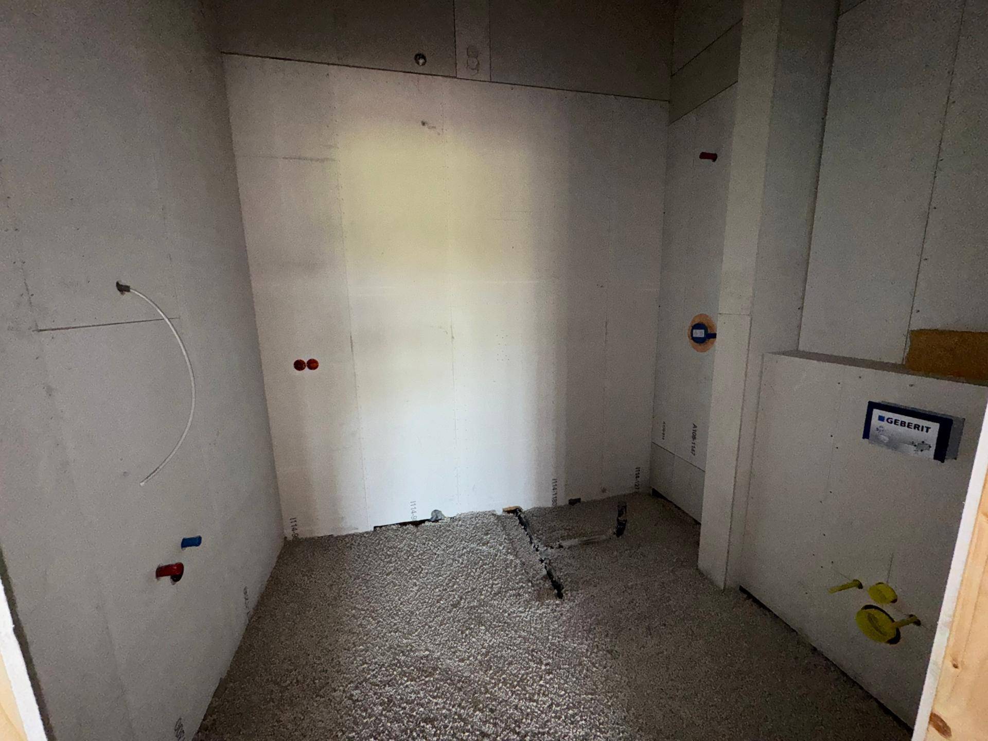 Kleiner Raum im Rohbau mit vorbereiteten Anschlüssen für ein WC und Waschbecken.