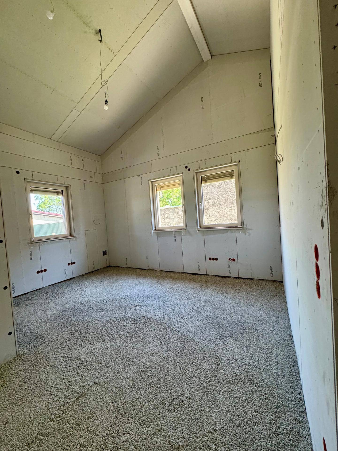 Helles Schlafzimmer im Rohbau mit drei Fenstern und viel natürlichem Licht.
