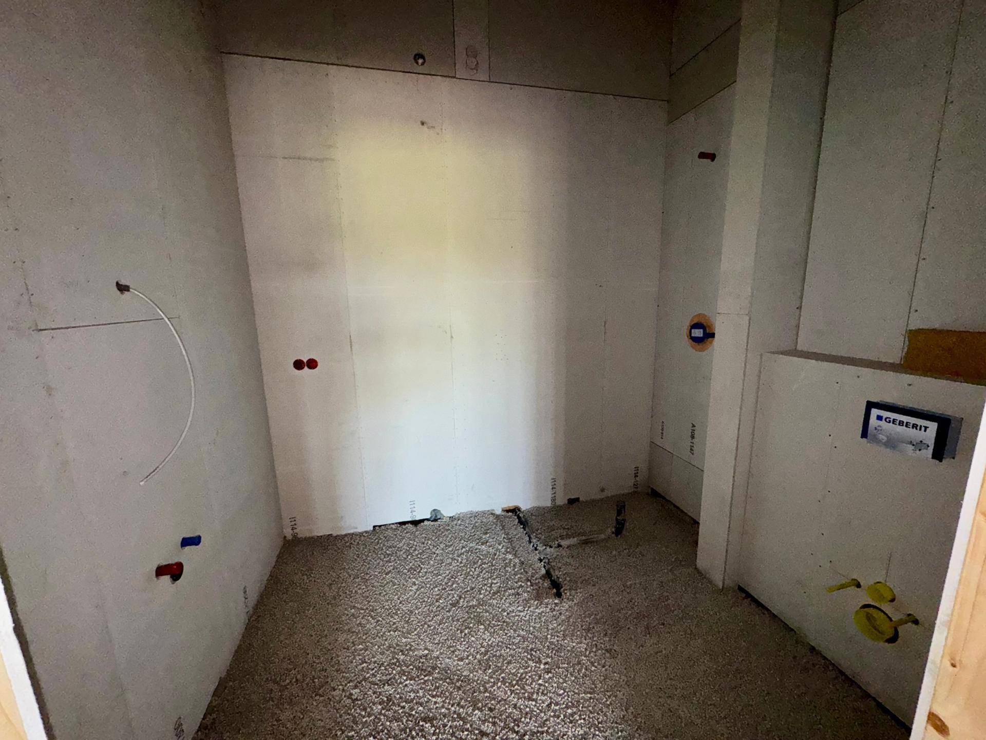 Badezimmer im Rohbau mit sichtbaren Wasserleitungen und Vorbereitung für Wandtoilette und Dusche.