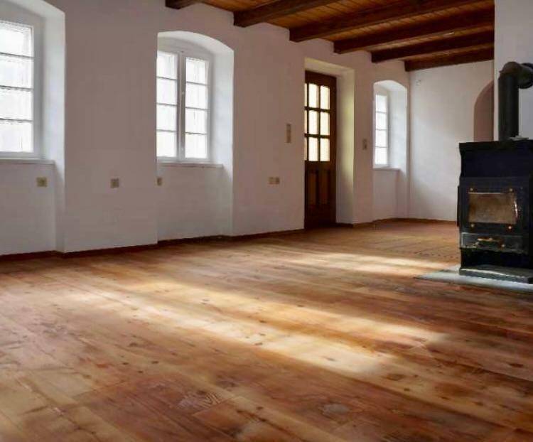 Geräumiges Wohnzimmer mit Holzboden, Holzbalkendecke und einem traditionellen Holzofen.