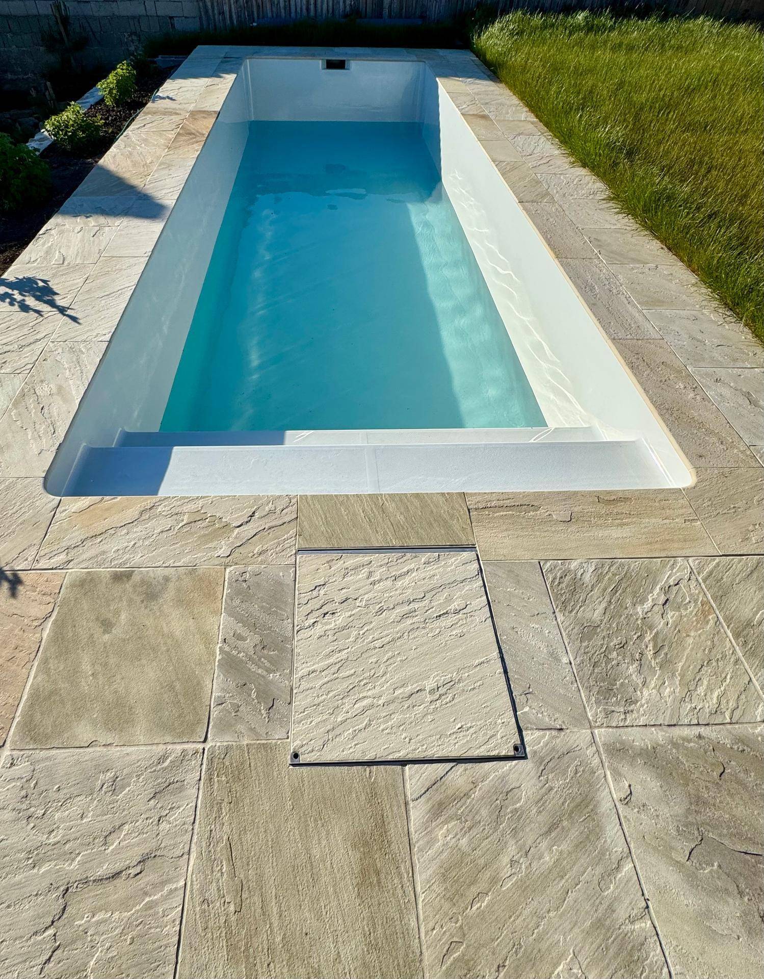 Neuer, rechteckiger Pool mit gefliestem Randbereich und klarem Wasser unter blauem Himmel.