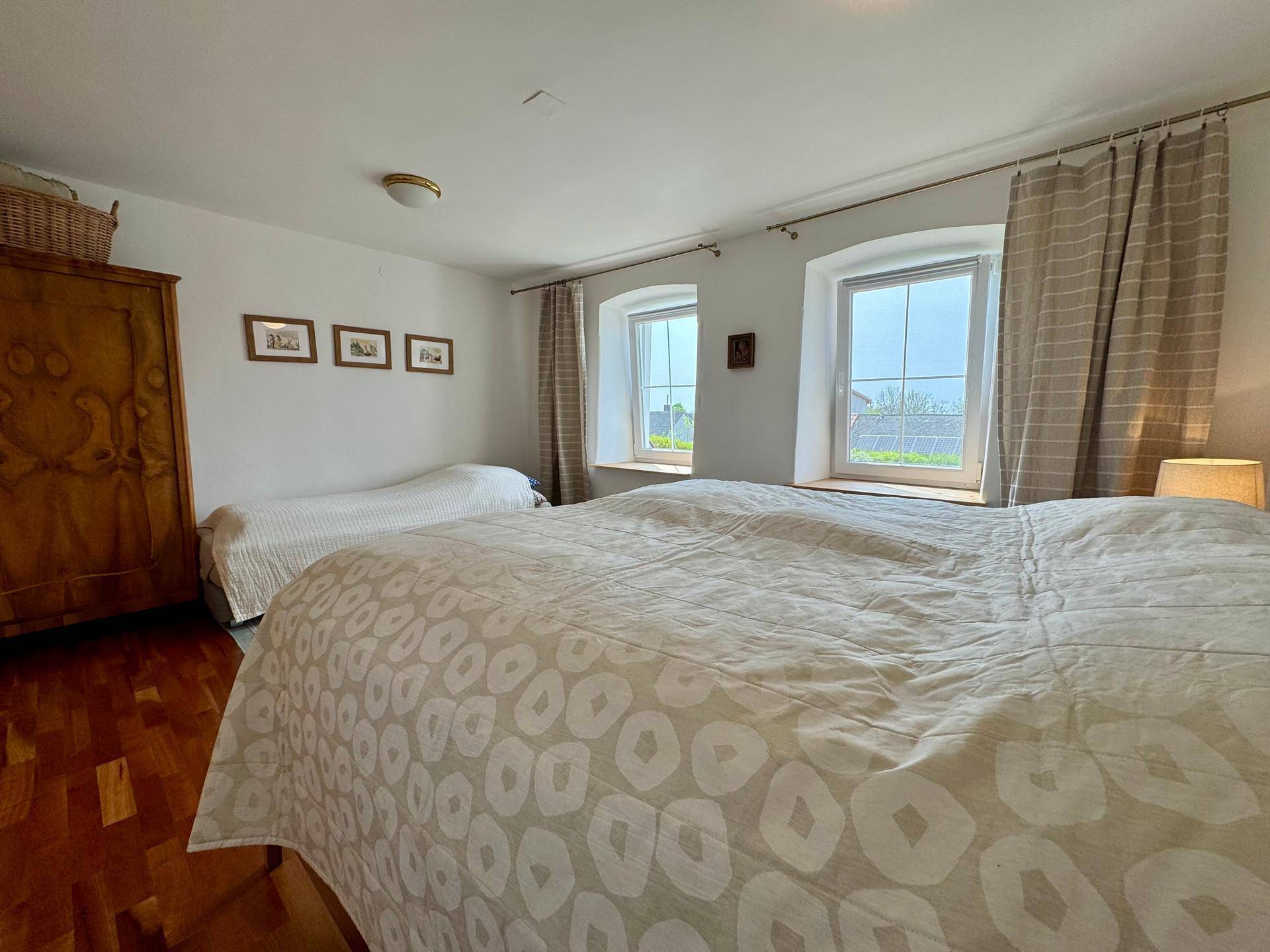 Helles Schlafzimmer mit Holzboden, zwei Betten und Blick ins Grüne, schafft eine gemütliche Atmosphäre.