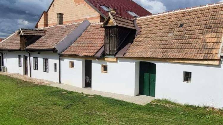 Langes, weißes Landhaus mit mehreren Fenstern und Türen, umgeben von Grünflächen.