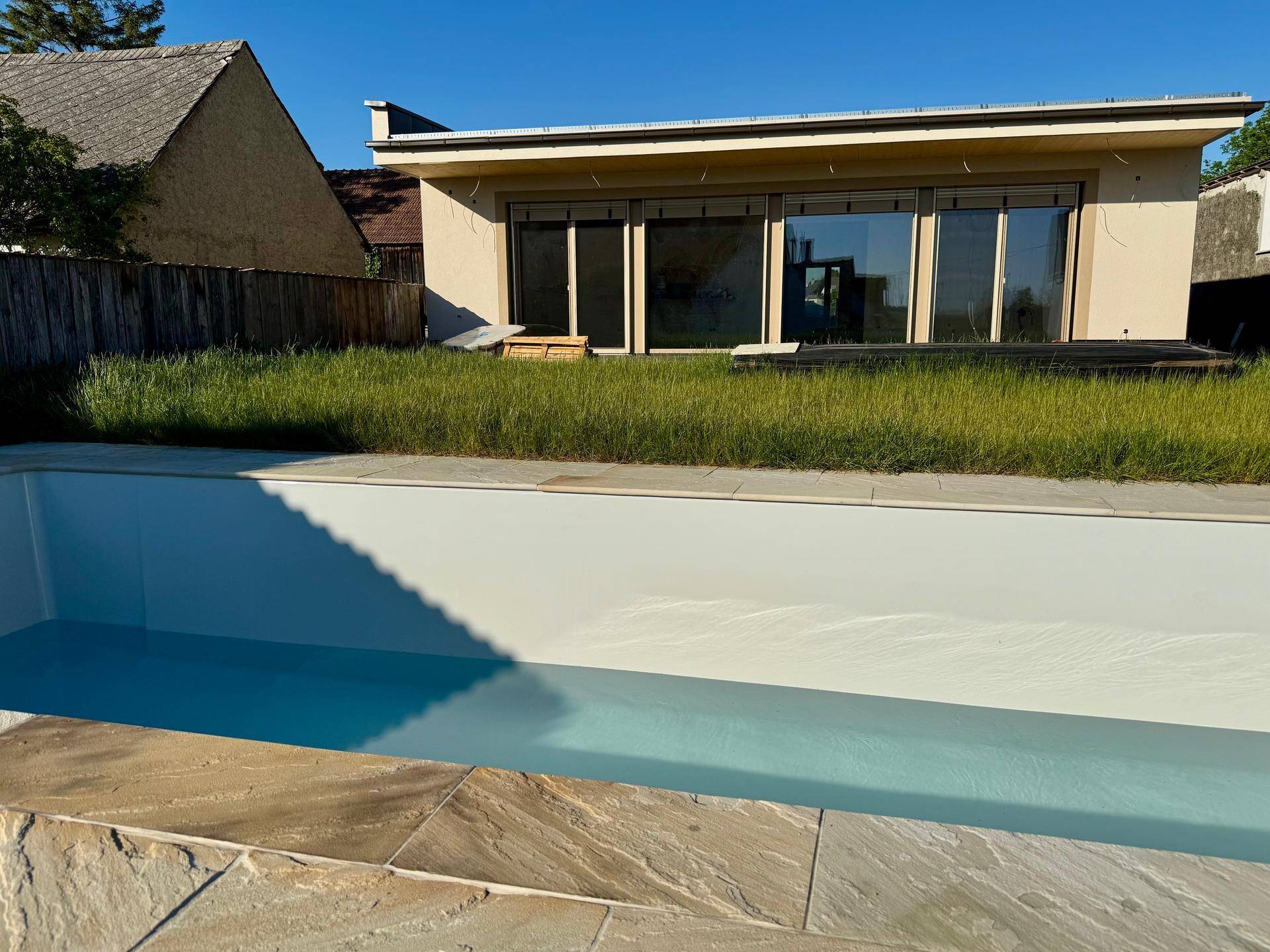 Außenbereich mit neuem Pool und Blick auf die moderne Hausfassade im Sonnenlicht.
