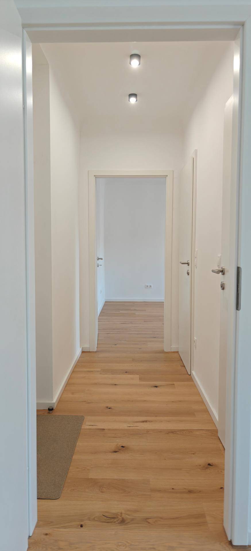 Heller Flur mit Holzparkettboden und mehreren Türen, der verschiedene Räume verbindet.