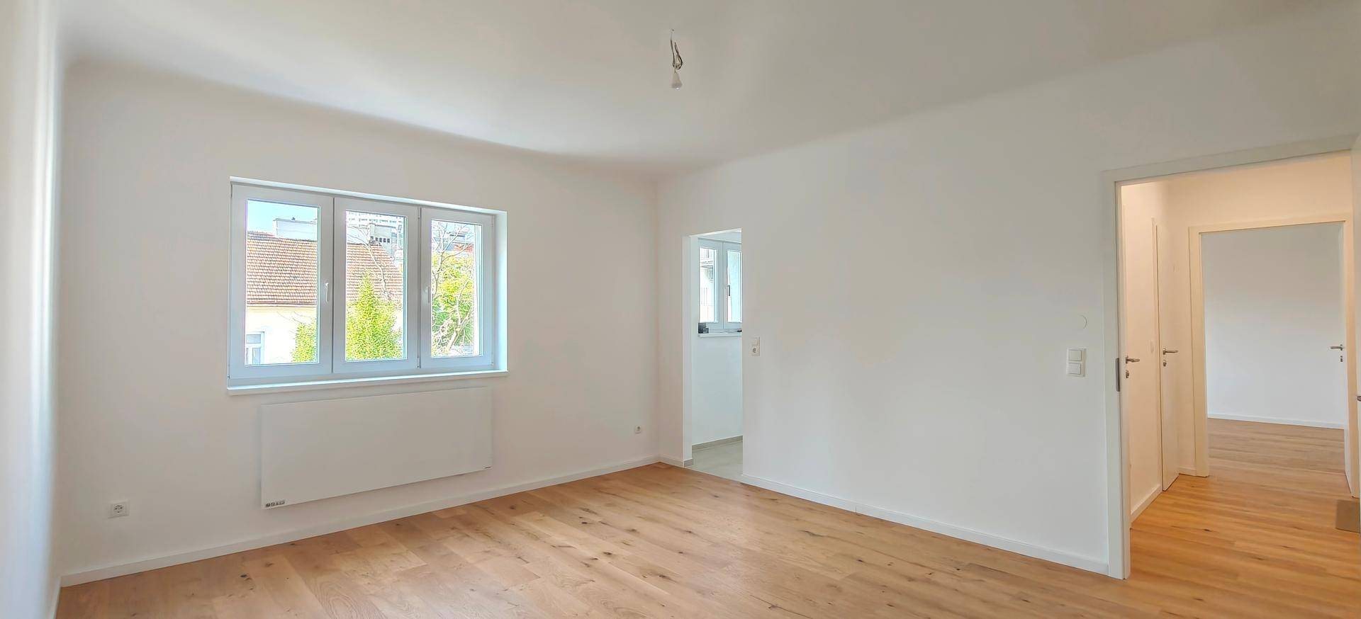 Geräumiges Zimmer mit hellem Holzparkett und Zugang zu weiteren Räumen, frisch renoviert.
