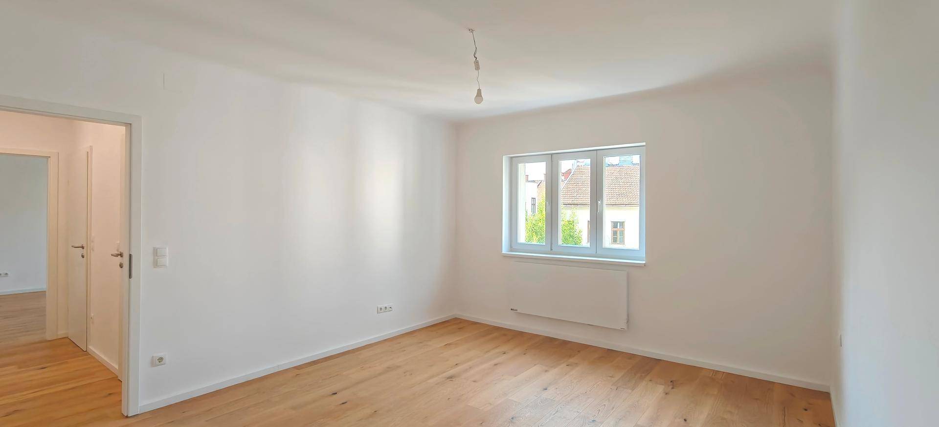 Helles Zimmer mit Zugang zu weiteren Räumen, ausgestattet mit modernem Holzparkett und weißen Wänden.