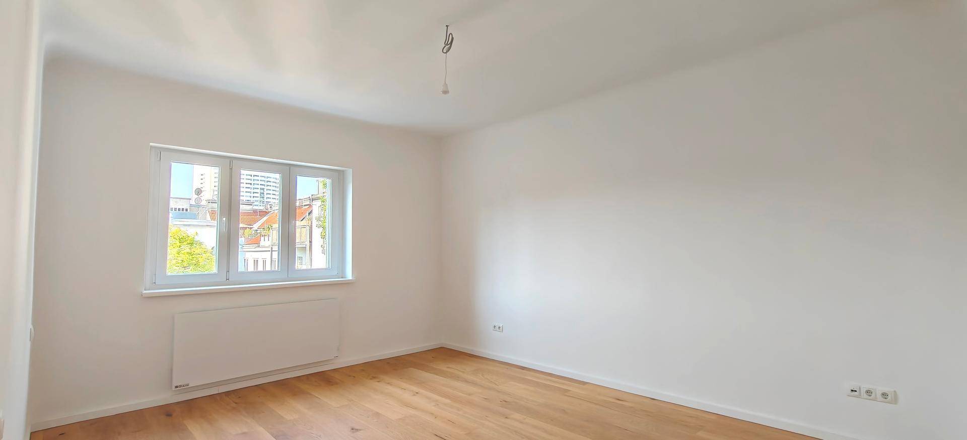 Unmöbliertes Schlafzimmer mit Holzboden und einem Fenster, das viel Tageslicht hereinlässt.