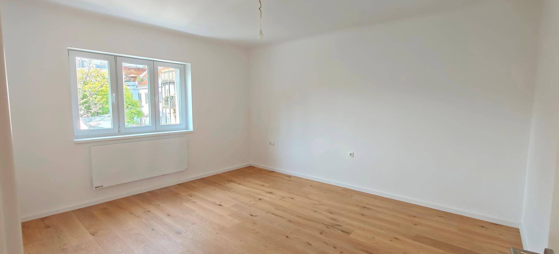 Freundliches Zimmer mit großen Fenstern und neu verlegtem Holzfußboden, bereit zum Einrichten.