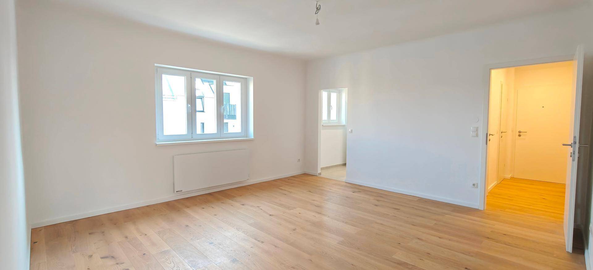 Geräumiges, unmöbliertes Zimmer mit Holzboden und Zugang zu einem hellen Flur.
