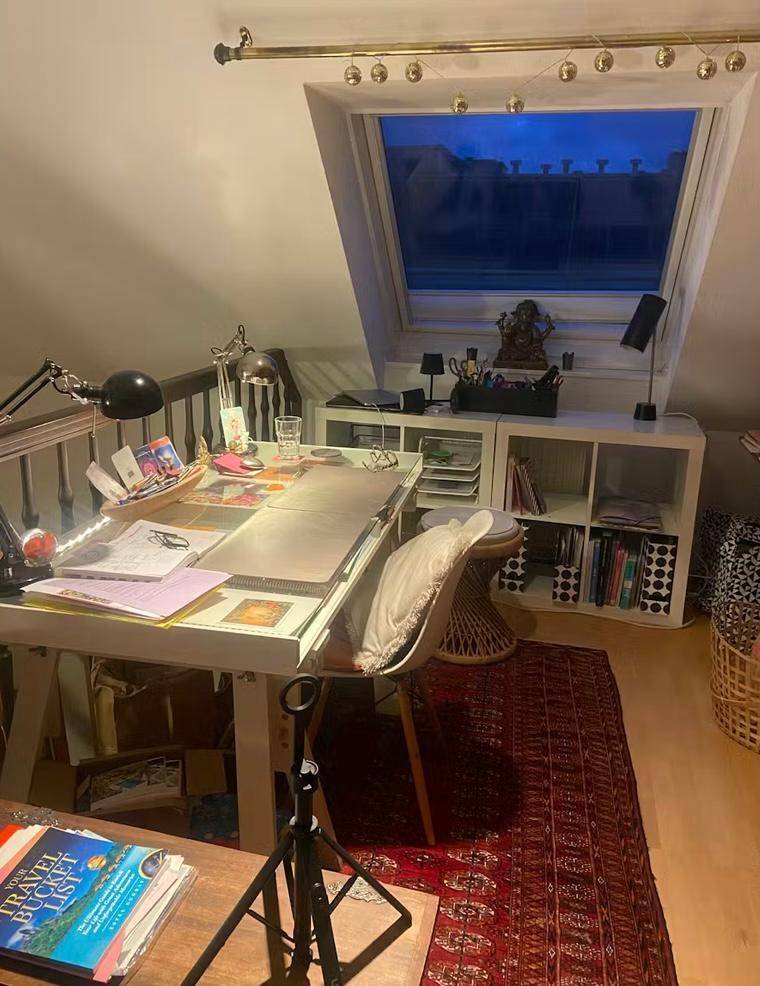 Gemütlicher Arbeitsplatz im Dachgeschoss mit Schreibtisch, Regalen und Dachfenster am Abend.