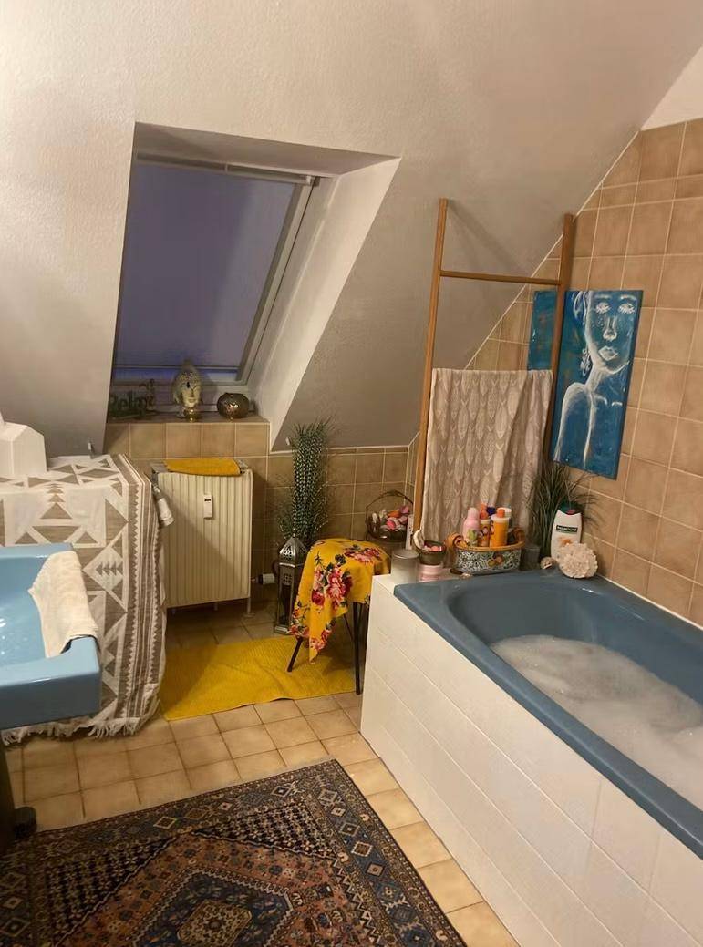 Badezimmer im Dachgeschoss mit Badewanne, Dachfenster und beigen Fliesenboden.