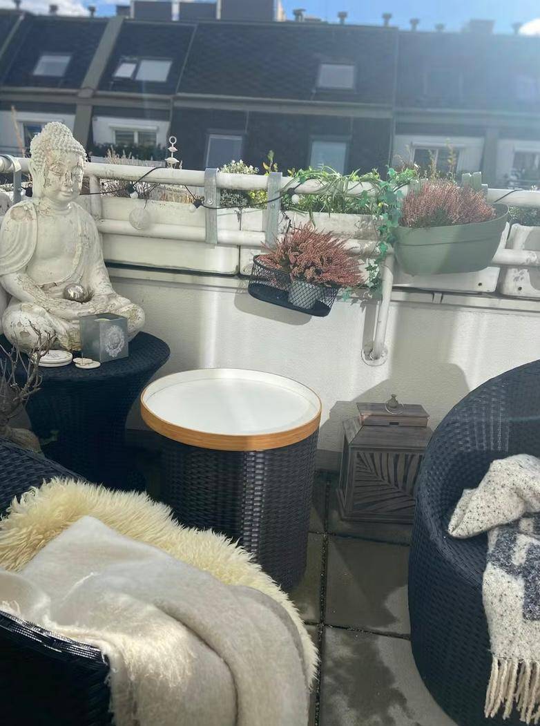 Sonniger Balkon mit bequemen Sitzgelegenheiten, Pflanzen und dekorativer Buddha-Statue.