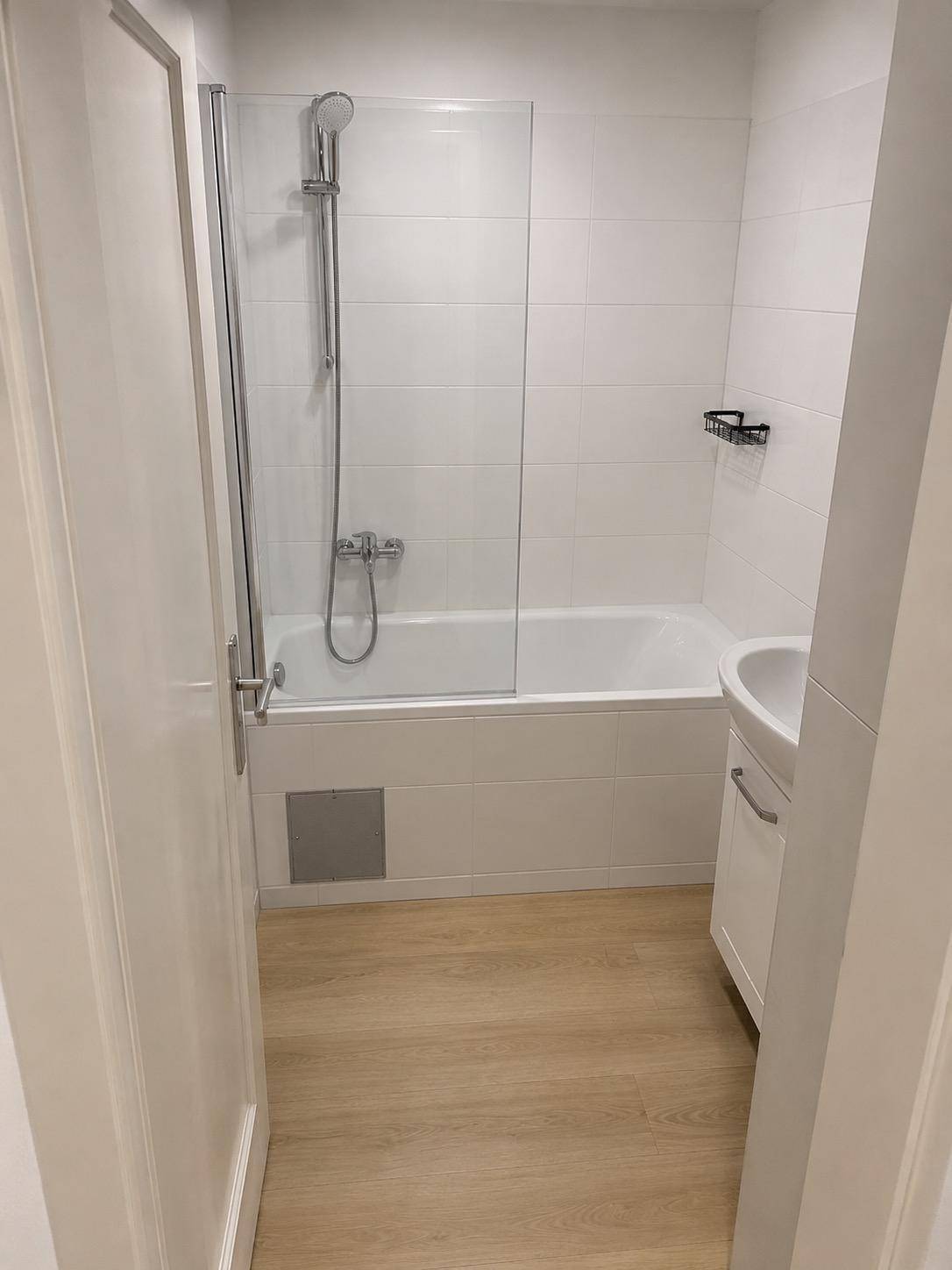 Helles Badezimmer mit Badewanne, Duschabtrennung, modernem Waschtisch und Laminatboden.