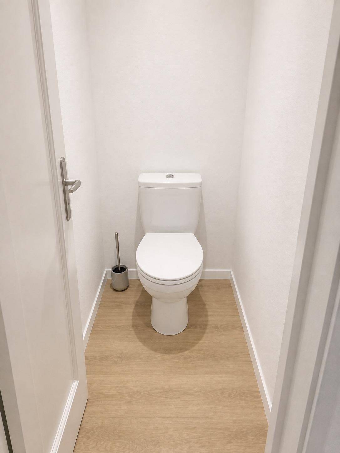 Separates WC mit weißer Toilette und hellem Laminatboden in einem schmalen, funktionalen Raum.