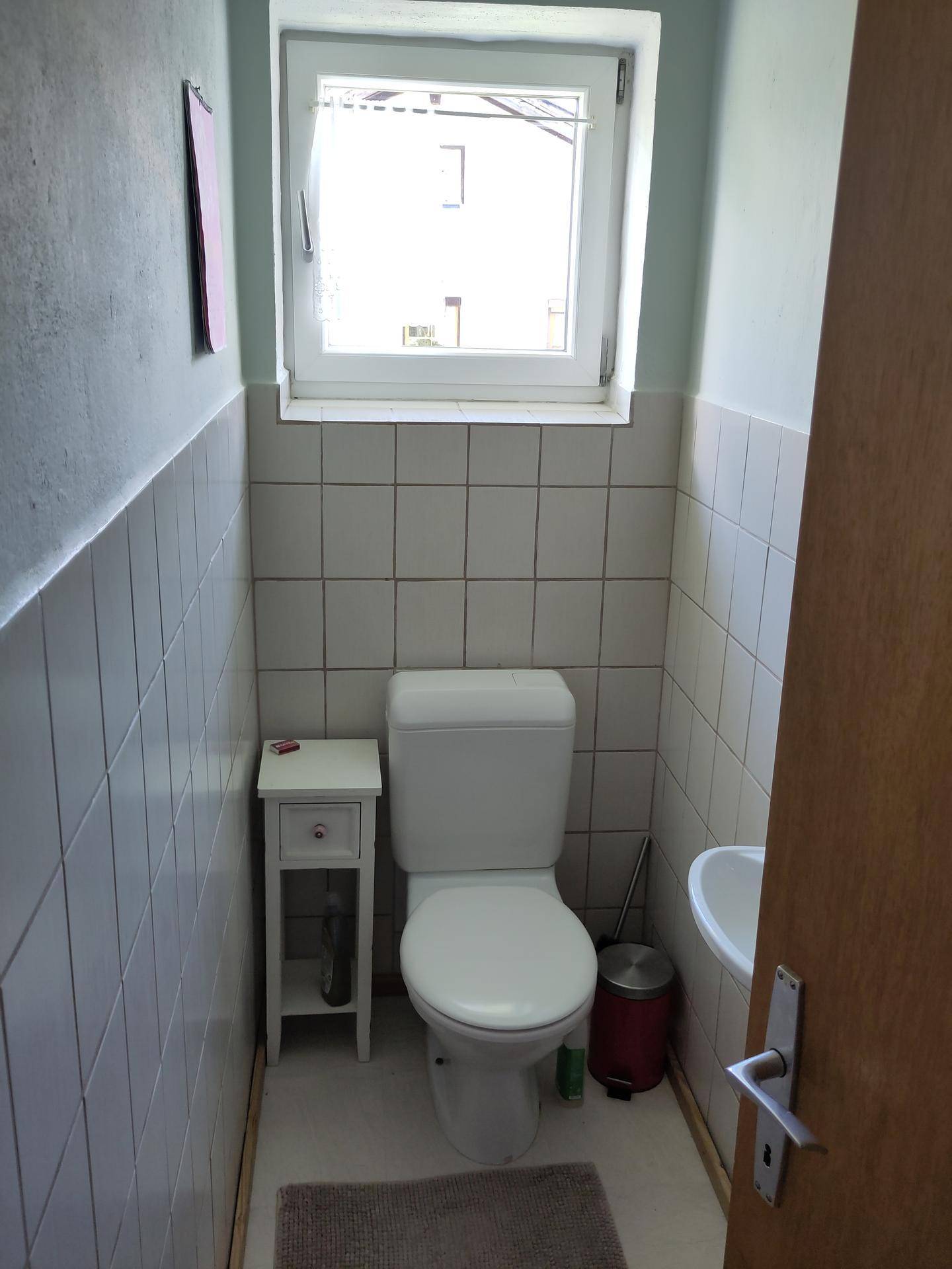Kleines Gäste-WC mit Fenster, weiß gefliesten Wänden und einfacher Ausstattung.