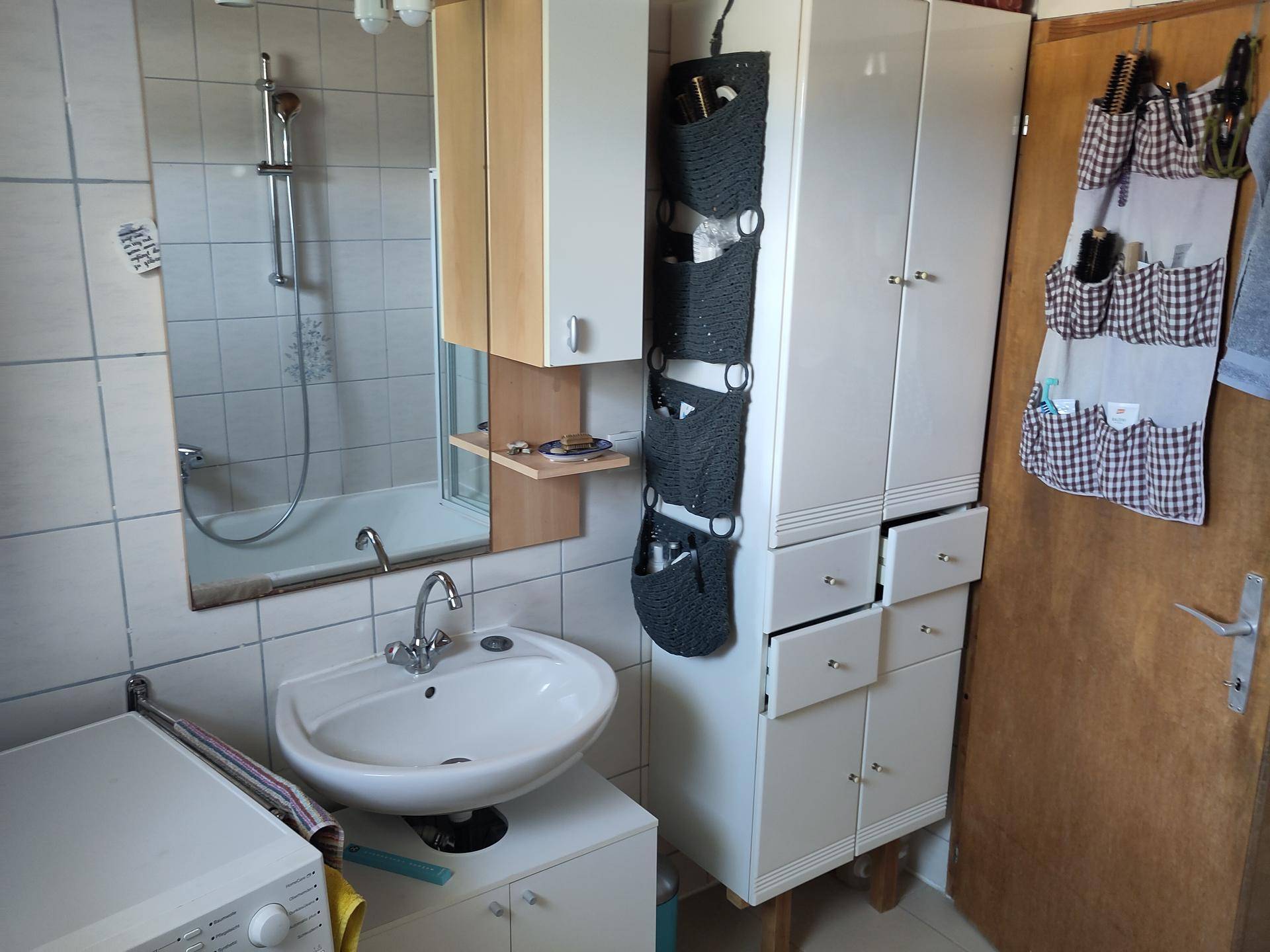 Funktionales Badezimmer mit Dusche, Waschbecken und Stauraum, hell gefliest.