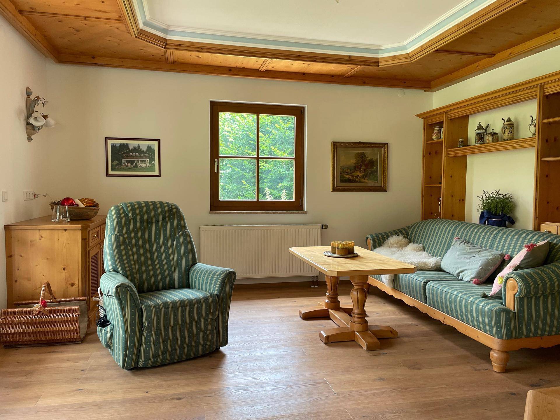 Traditionelles Wohnzimmer mit Holzdecke, bequemen Möbeln und Blick ins Grüne.