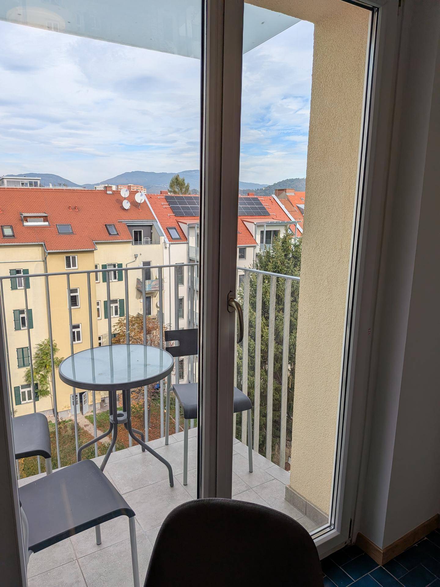 Balkon mit Sitzgelegenheiten und weitem Blick über Dächer und Berge.