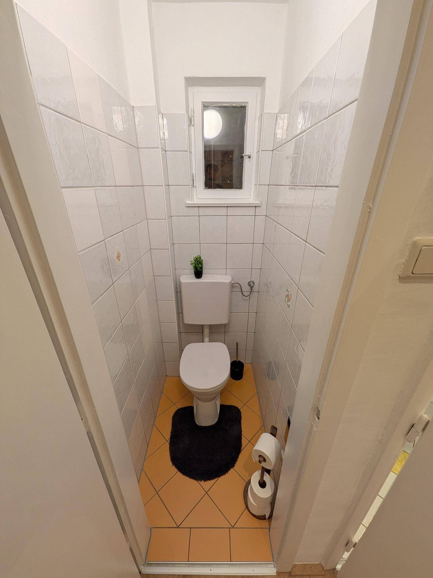 Separates WC mit Fenster, weißen Wandfliesen und Terrakotta-Bodenfliesen.