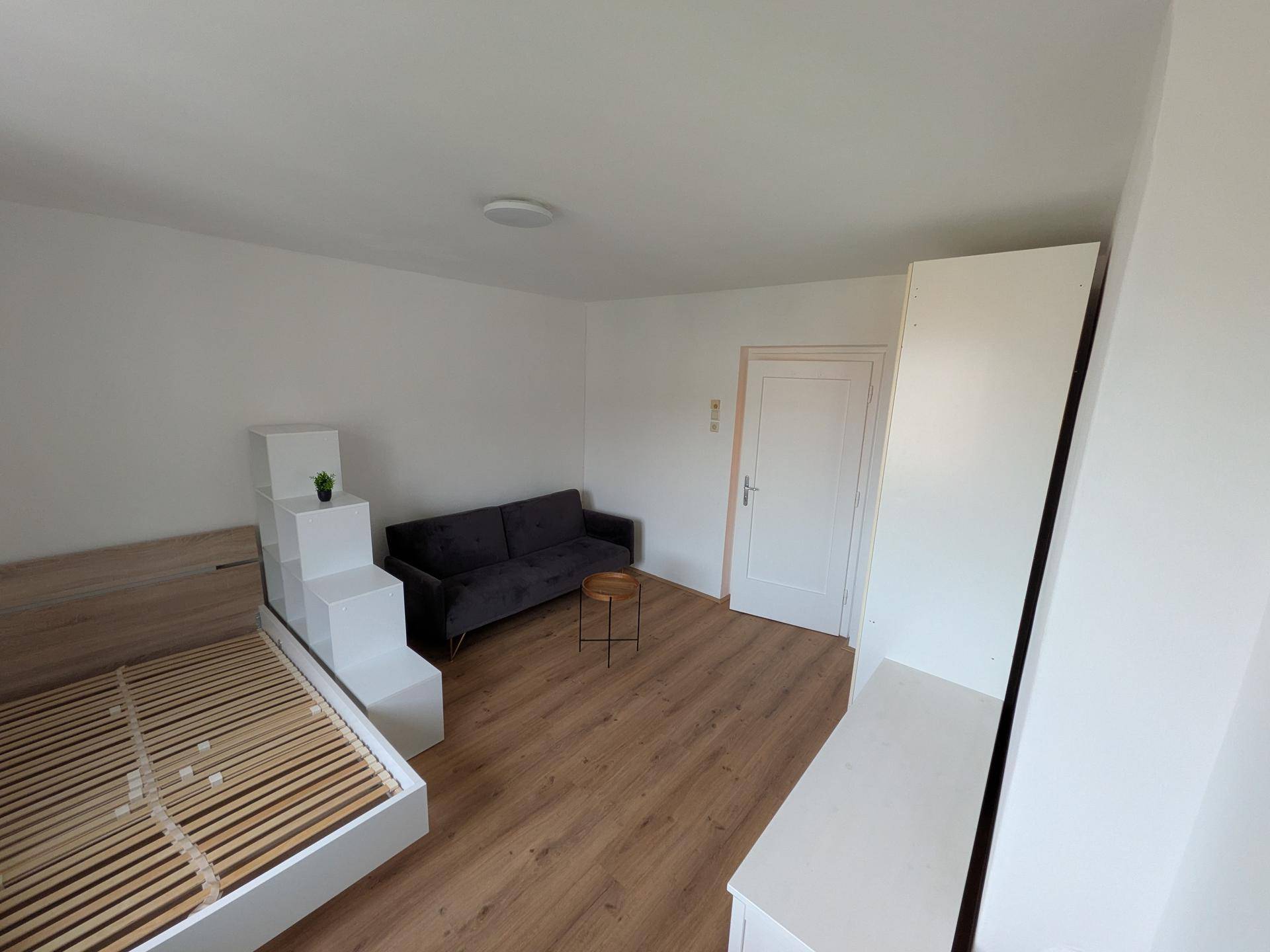 Gemütlicher Wohnbereich mit Bettgestell, Sofa und hellem Laminatboden.