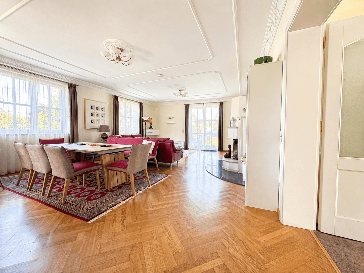 Geräumiger Wohn-Essbereich mit Fischgrätparkett, Stuckdecken und eleganten Möbeln.