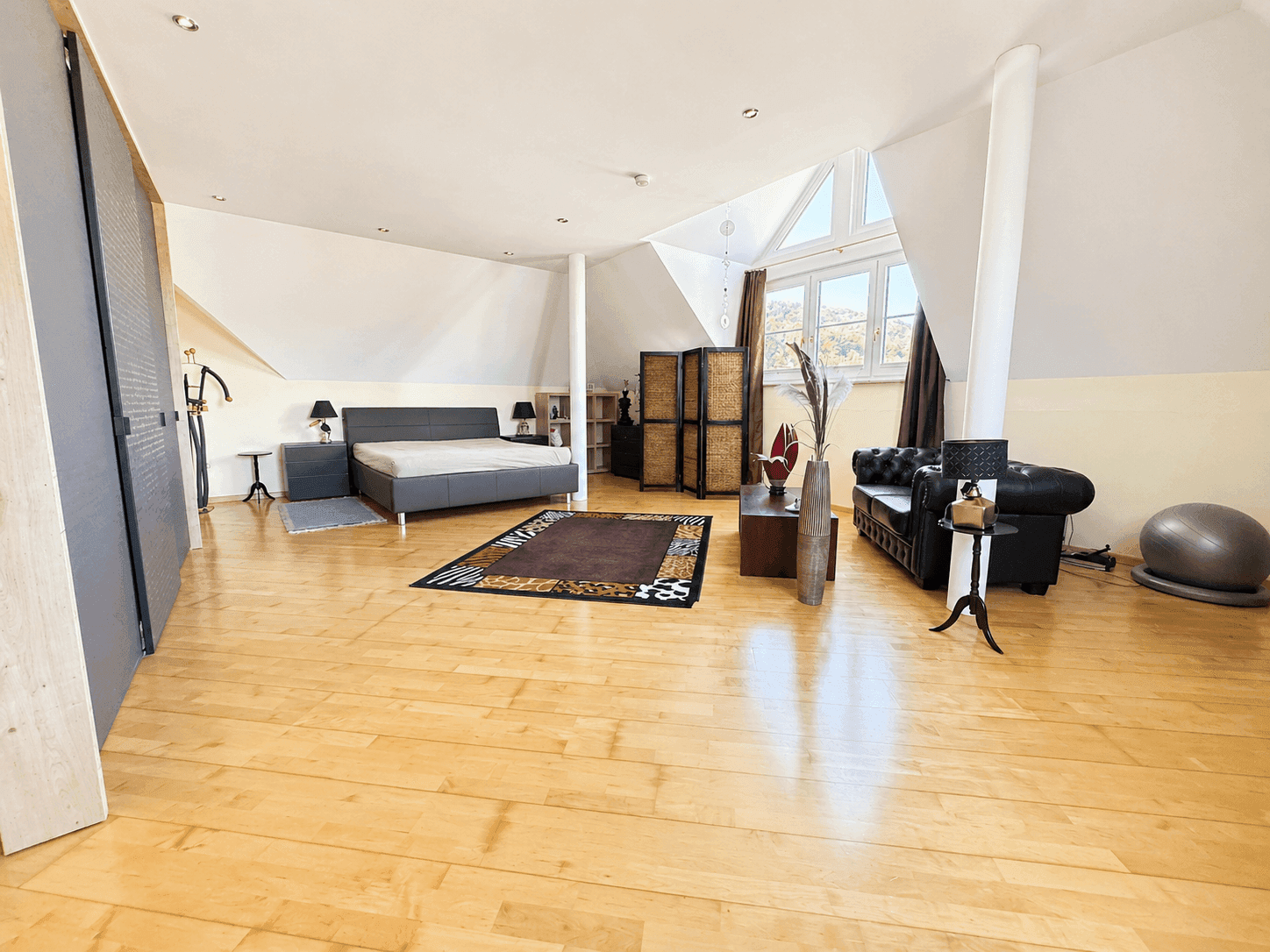 Helles Schlafzimmer im Dachgeschoss mit Holzboden, großem Fenster und Sitzbereich.