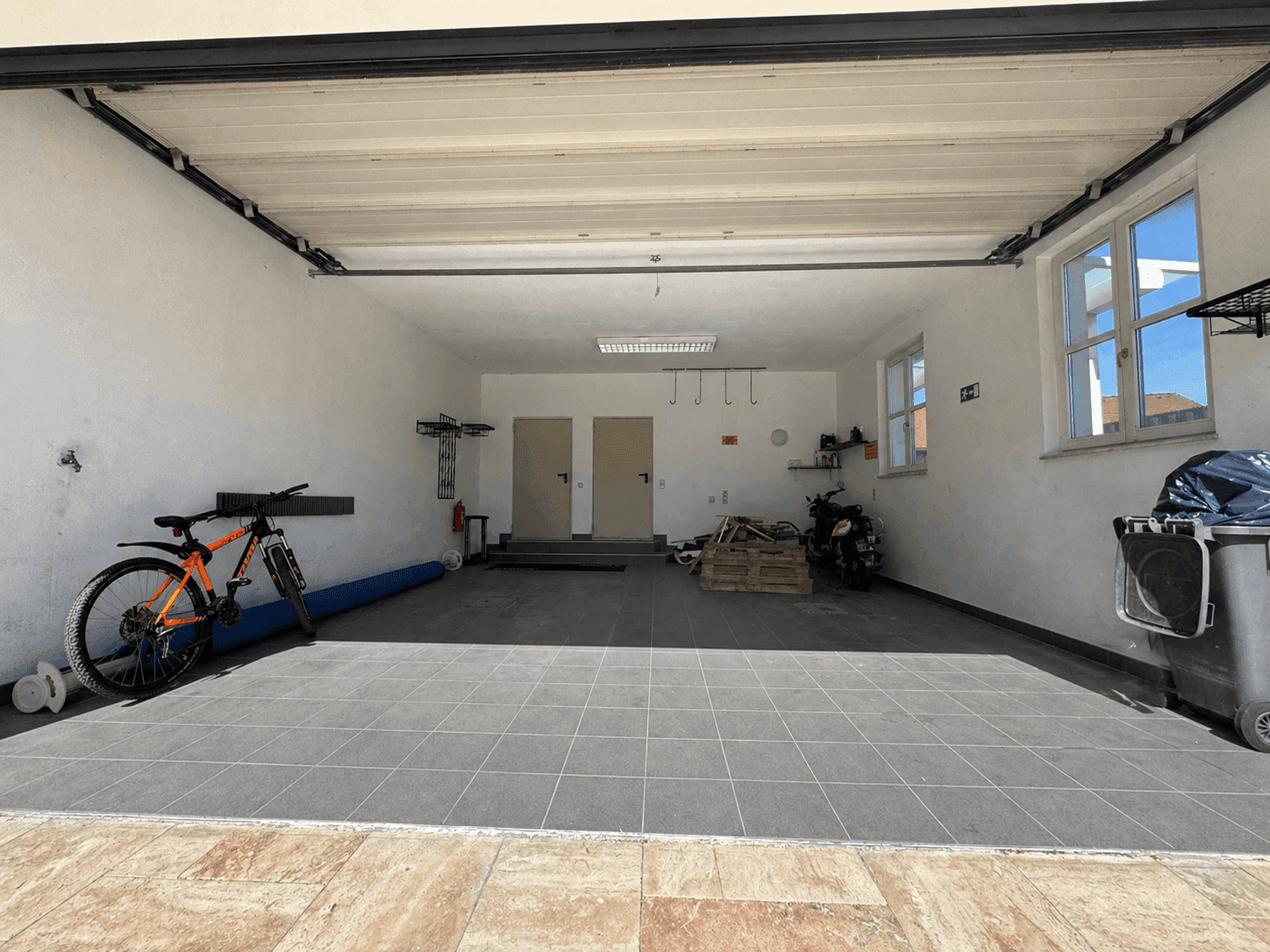 Geräumige Garage mit Fliesenboden, Fenstern und Platz für Fahrräder und Fahrzeuge.