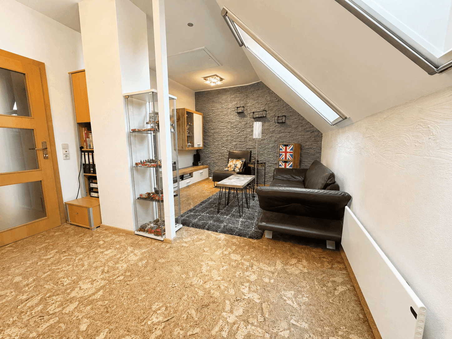 Gemütliches Wohnzimmer im Dachgeschoss mit Schrägdach, Steinwand und Holzboden.