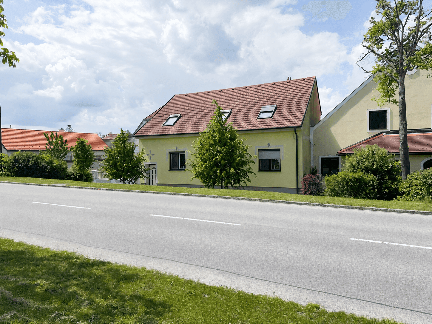 Ansicht des gelben Hauses von der Straße aus mit Satteldach und Dachfenstern.