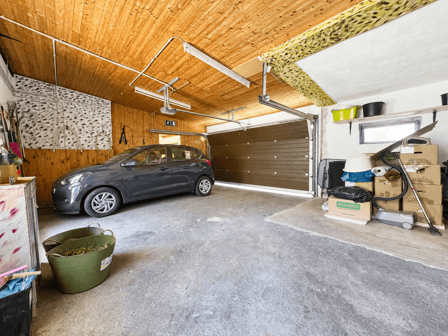 Geräumige Garage mit Betonboden, Holzdecke und Platz für ein Fahrzeug sowie Abstellmöglichkeiten.