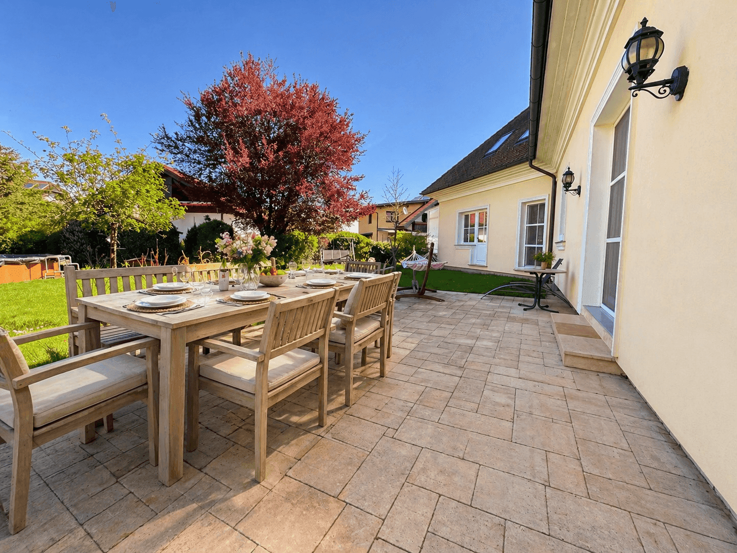 Große gepflasterte Terrasse mit Esstisch, Gartenmöbeln und Blick ins Grüne.