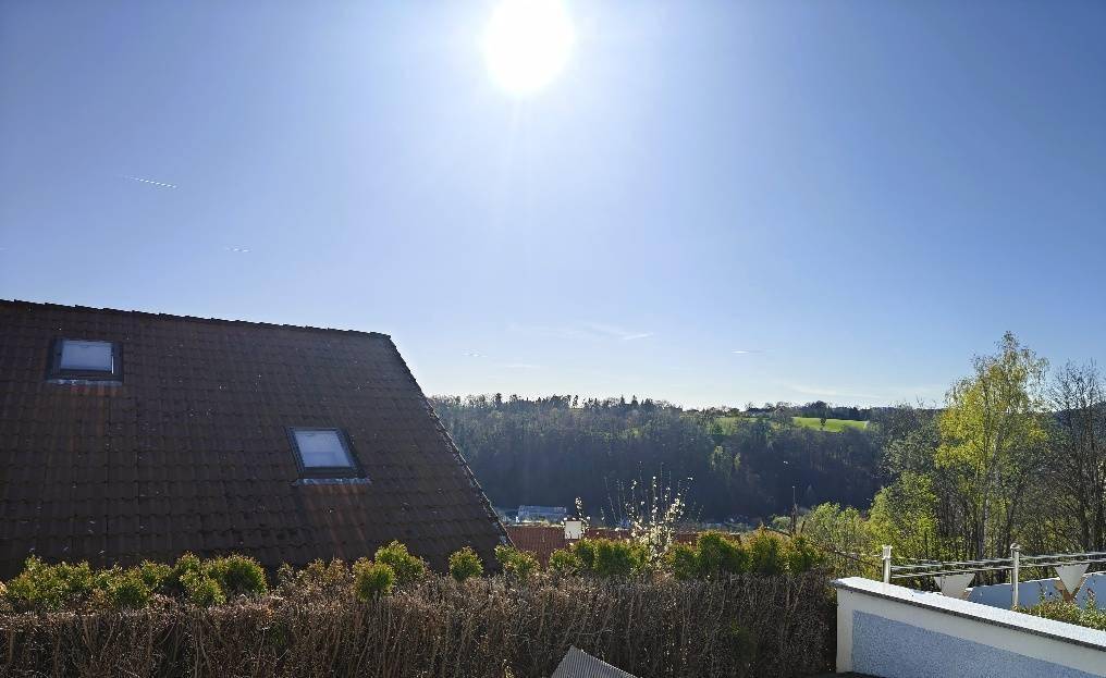 Sonniger Ausblick auf die hügelige Landschaft und ein Dach mit Dachfenstern.