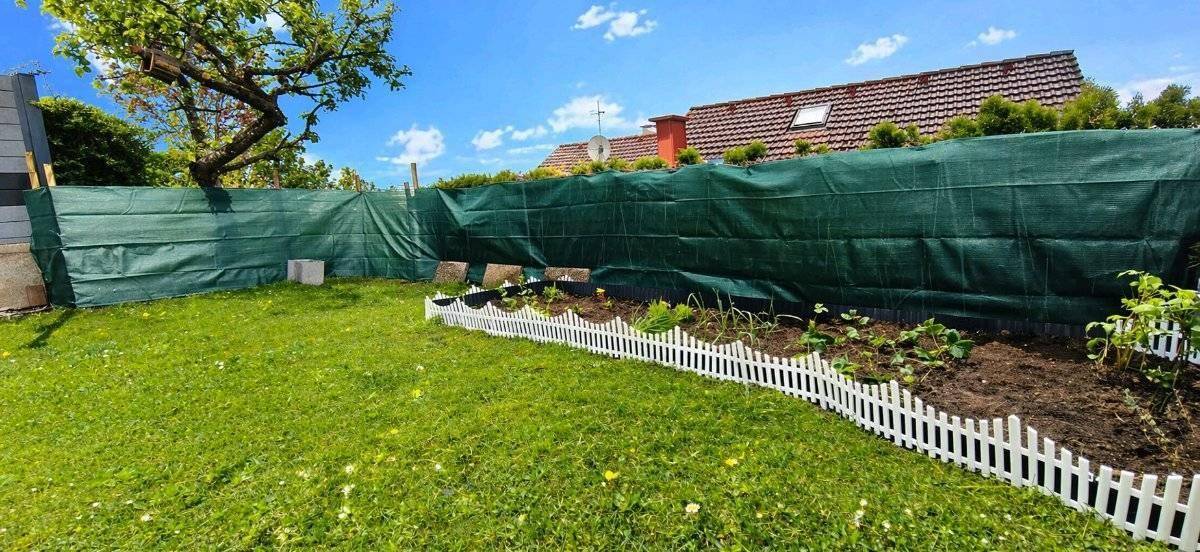 Gepflegter Gartenbereich mit Rasenfläche, Beeten und einem kleinen Zaun.
