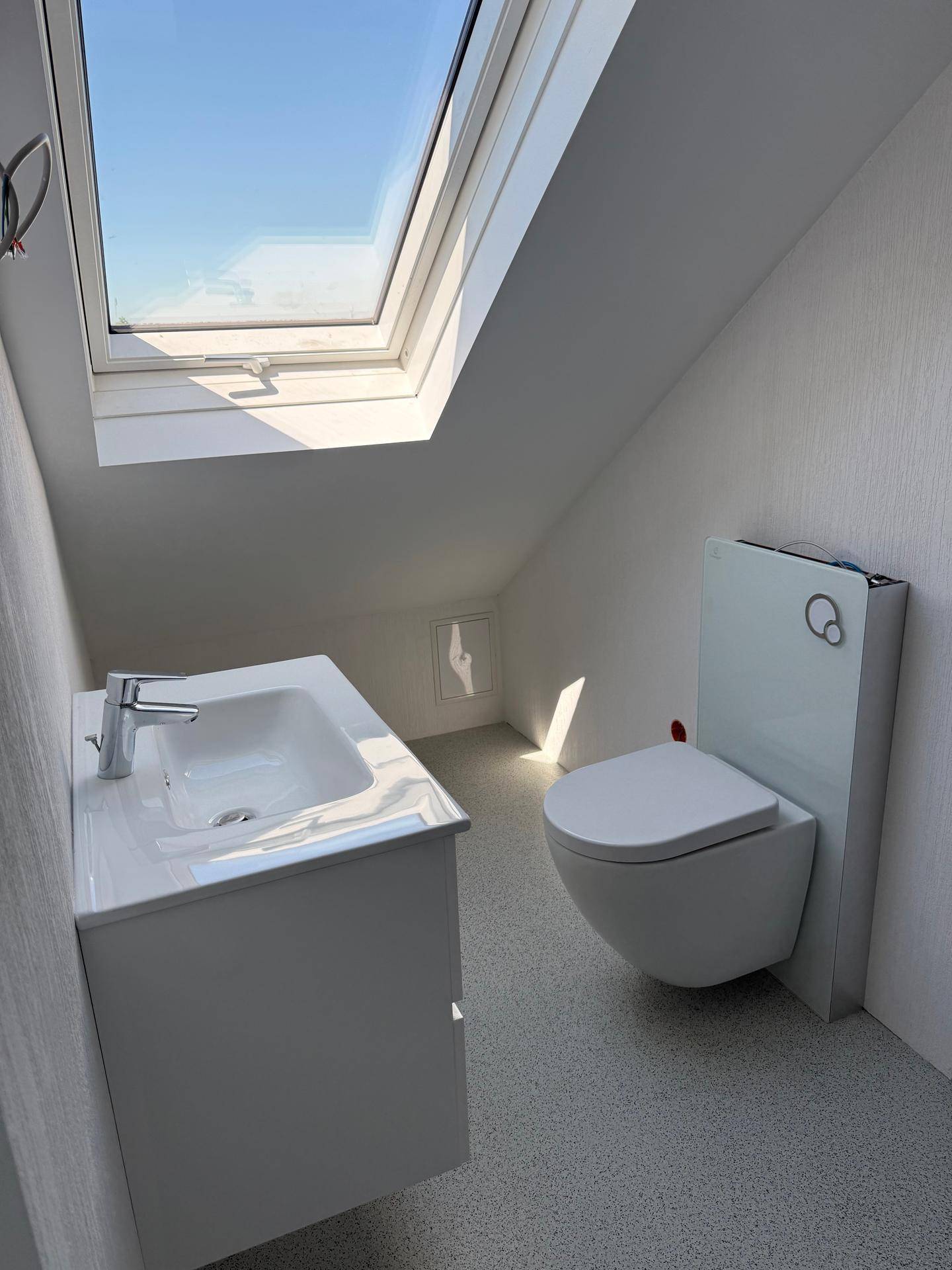 Helles Badezimmer im Dachgeschoss mit Waschtisch, Toilette und großem Dachfenster.