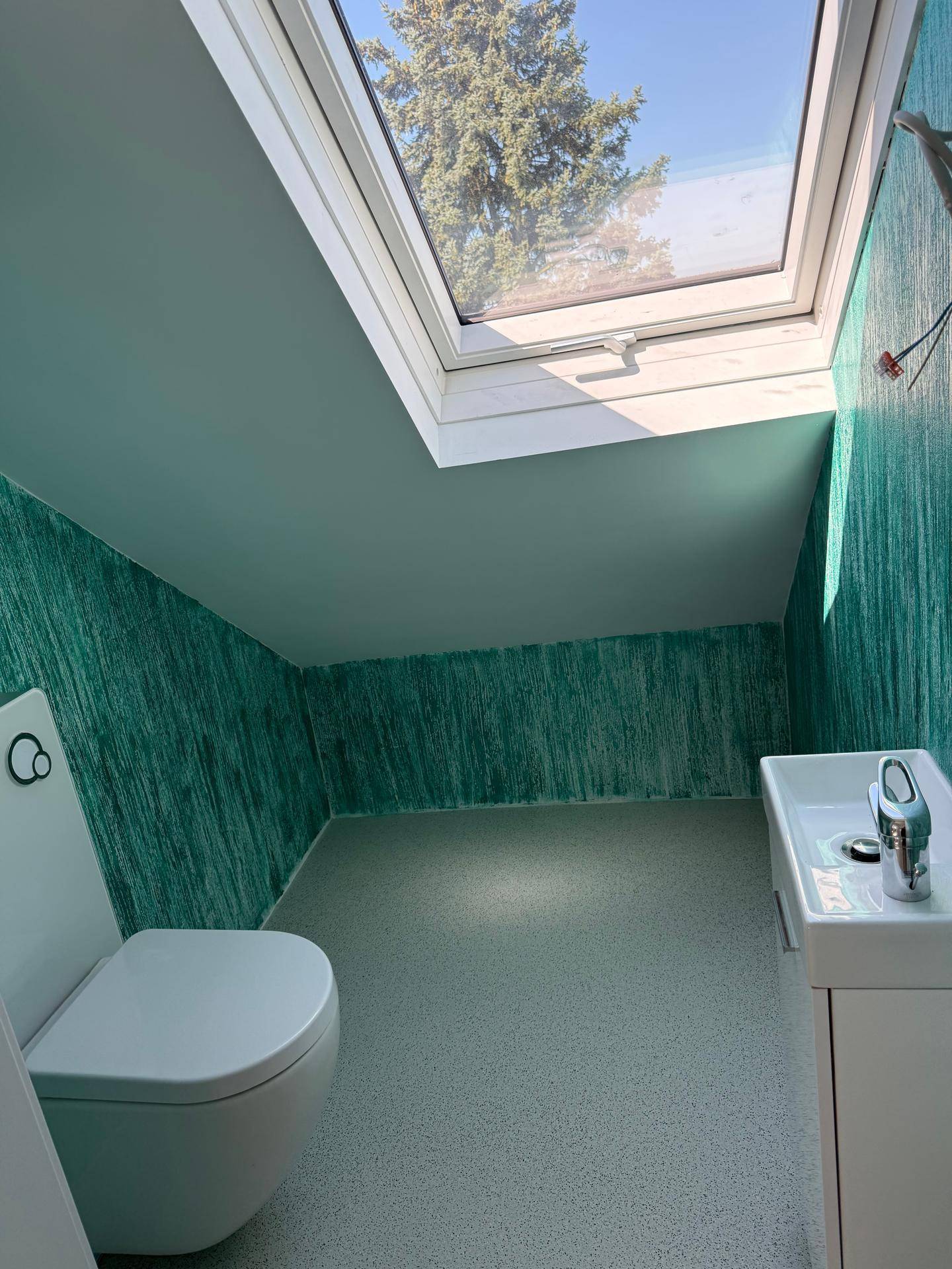 Kleines WC im Dachgeschoss mit Waschtisch, Toilette, Dachfenster und grüner Wandgestaltung.