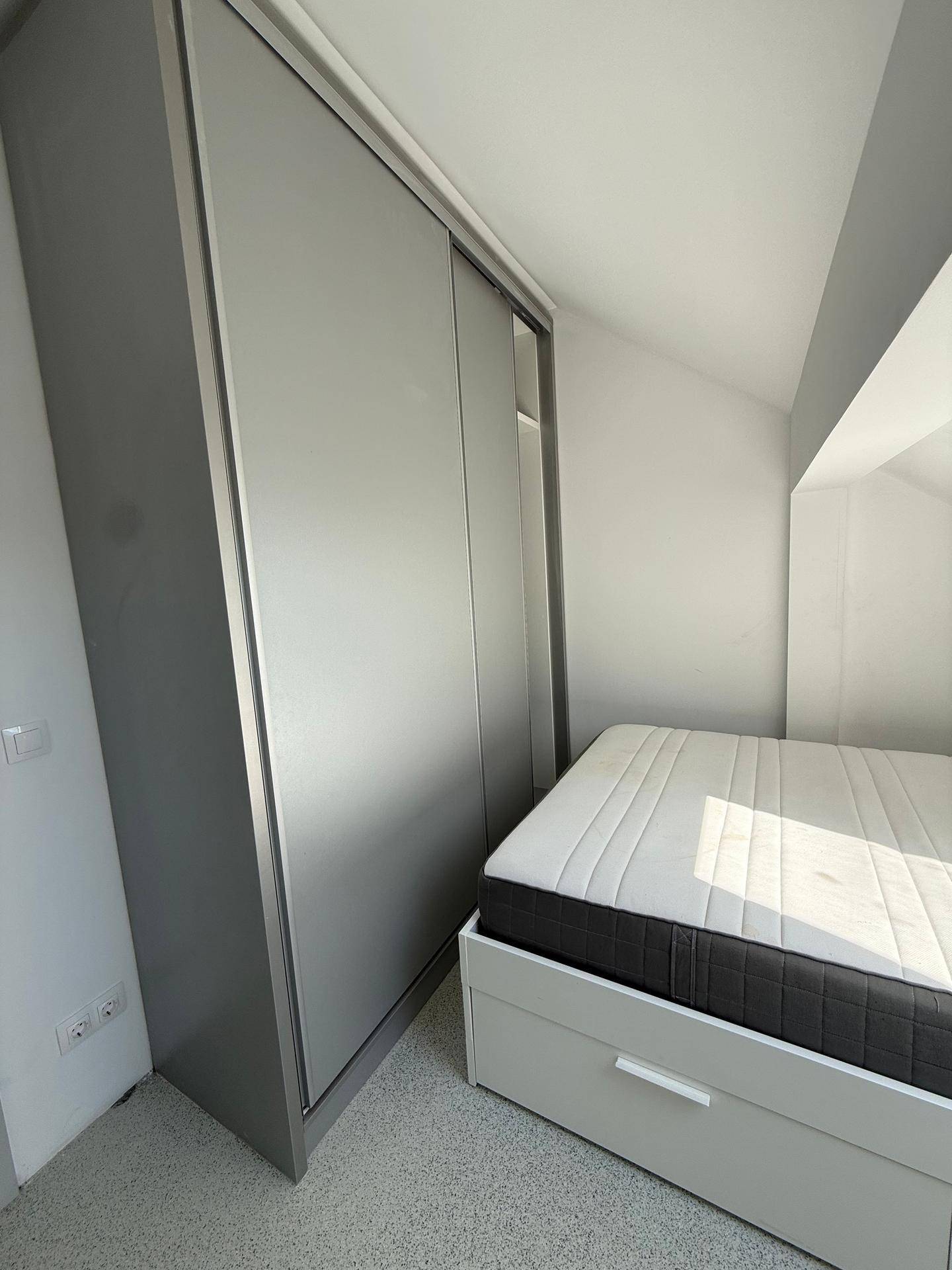 Schlafzimmer im Dachgeschoss mit Einbauschrank, Bett und schrägen Wänden.