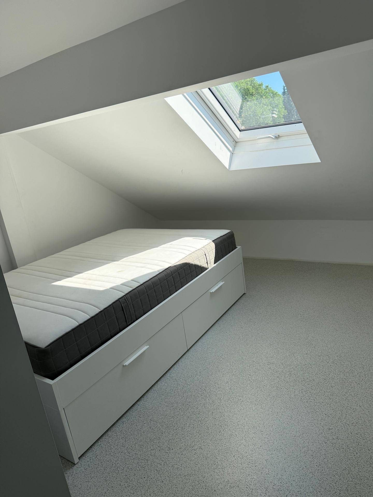 Helles Schlafzimmer im Dachgeschoss mit Bett, Stauraum und einem großen Dachfenster.