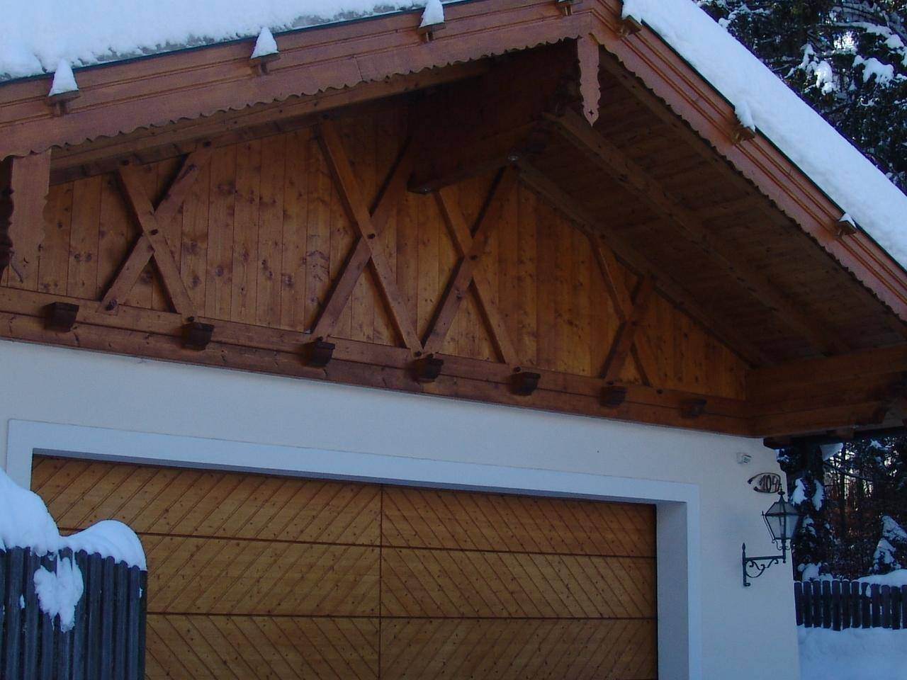 Holzgarage mit dekorativem Giebel und schneebedecktem Dachvorsprung, passend zum alpinen Stil.
