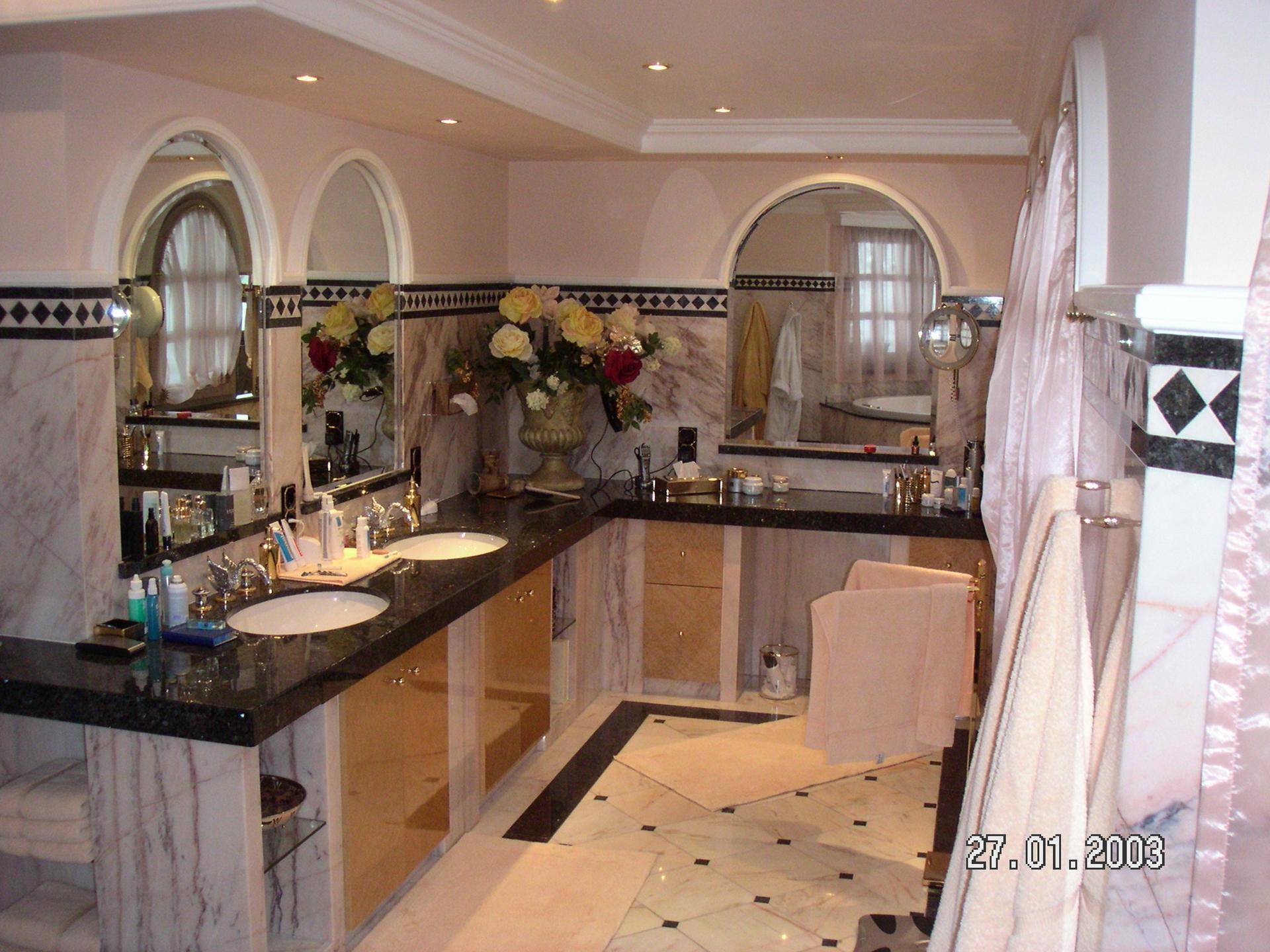 Elegantes Badezimmer mit Doppelwaschbecken, Marmoroberflächen und dekorativen Bogenfenstern.
