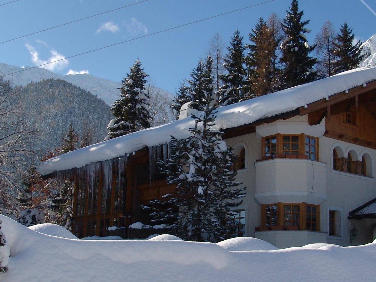 Idyllisches Haus in winterlicher Landschaft mit schneebedecktem Dach und alpiner Umgebung.