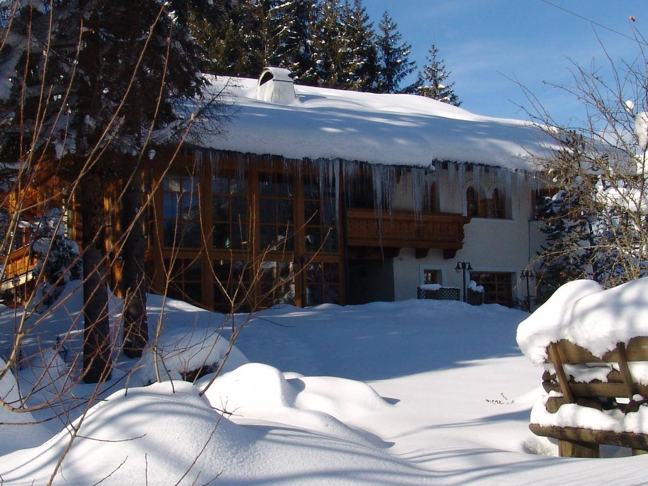 Traditionelles Haus im Winter mit schneebedecktem Dach und Eiszapfen, umgeben von Bäumen.