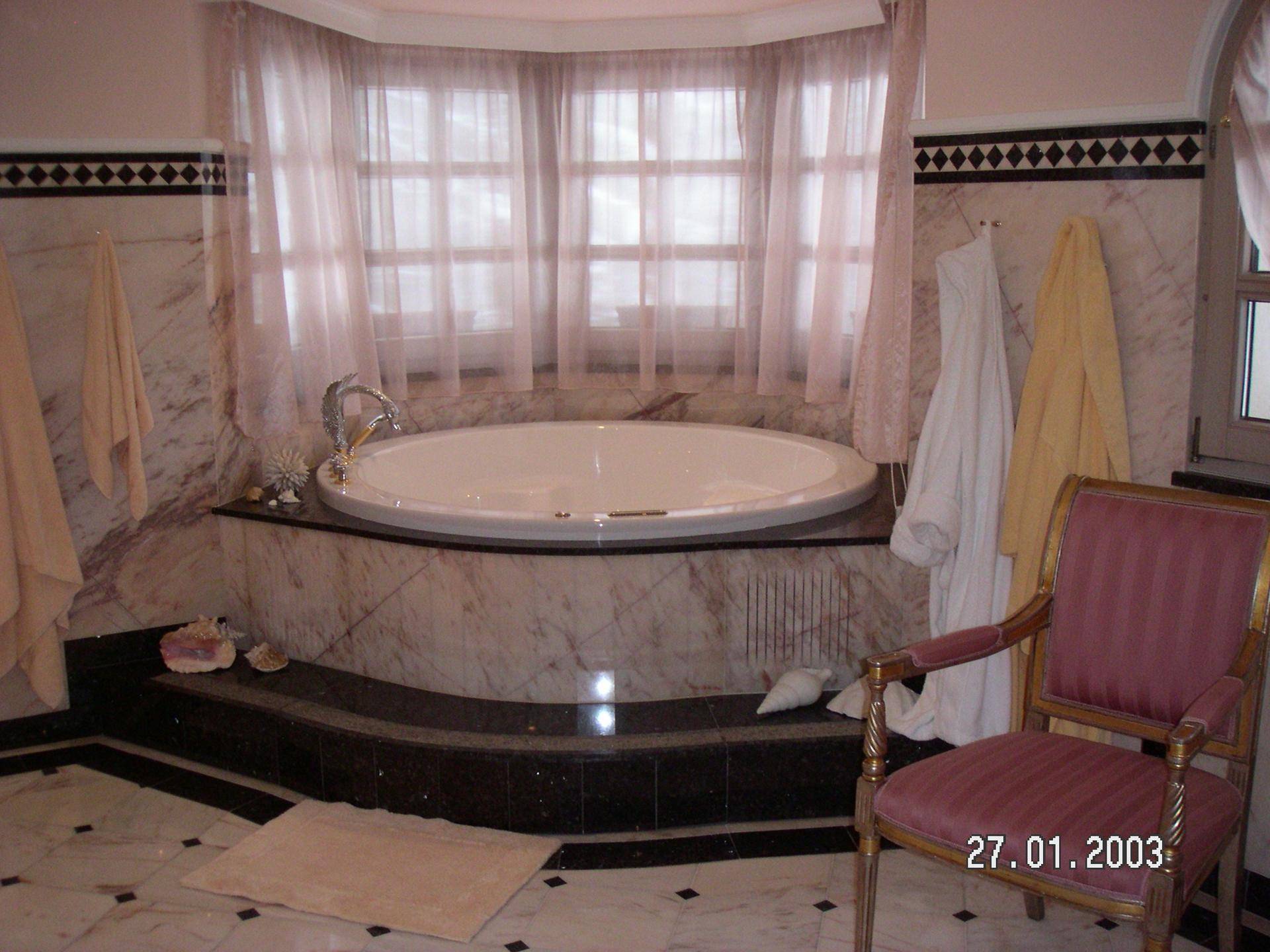 Luxuriöses Badezimmer mit runder Badewanne, Marmorverkleidung und großen Fenstern.