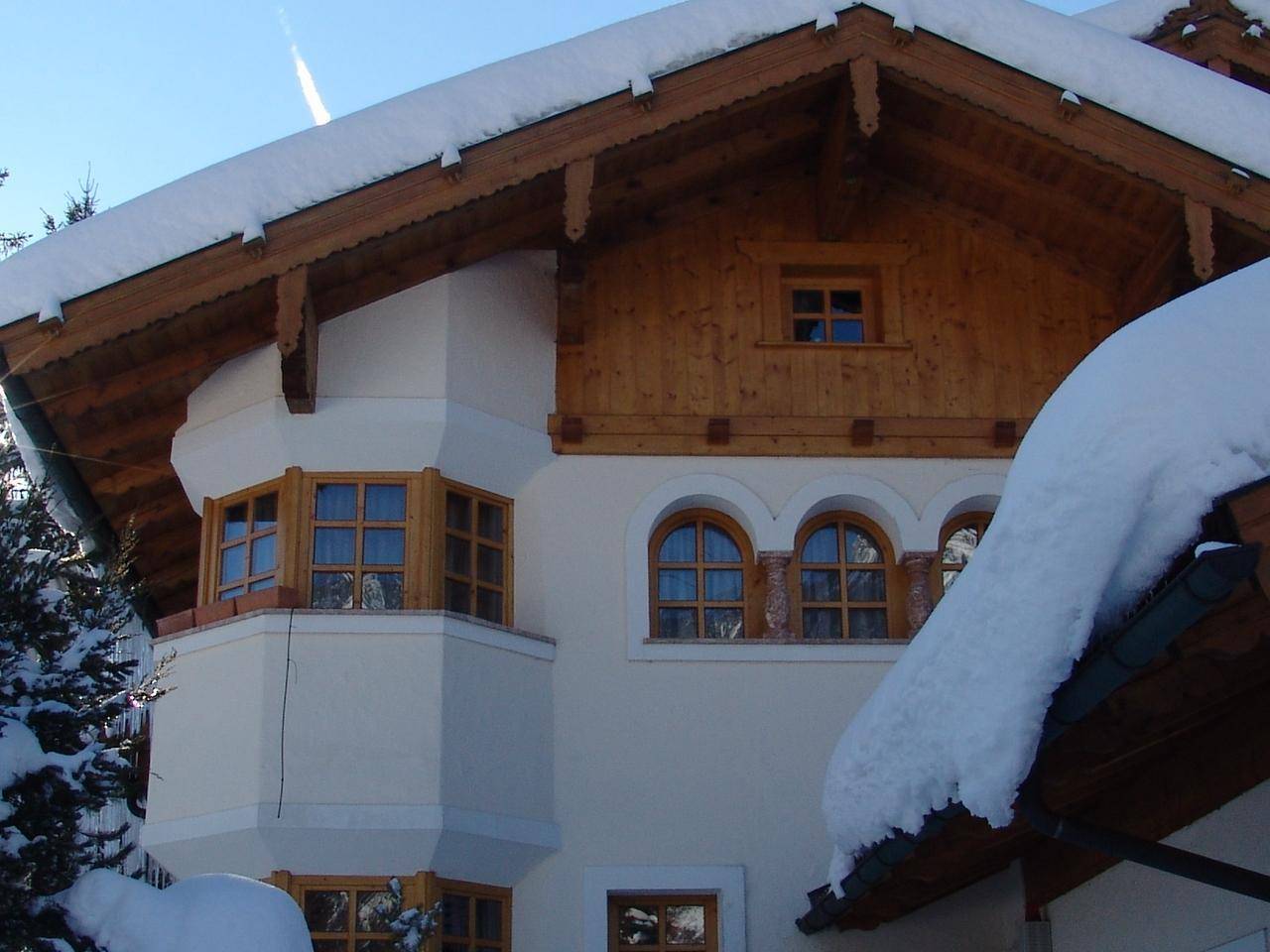 Detailansicht der Hausfassade mit Erkerfenstern, Rundbogenfenstern und dekorativen Holzelementen unter dem Dach.
