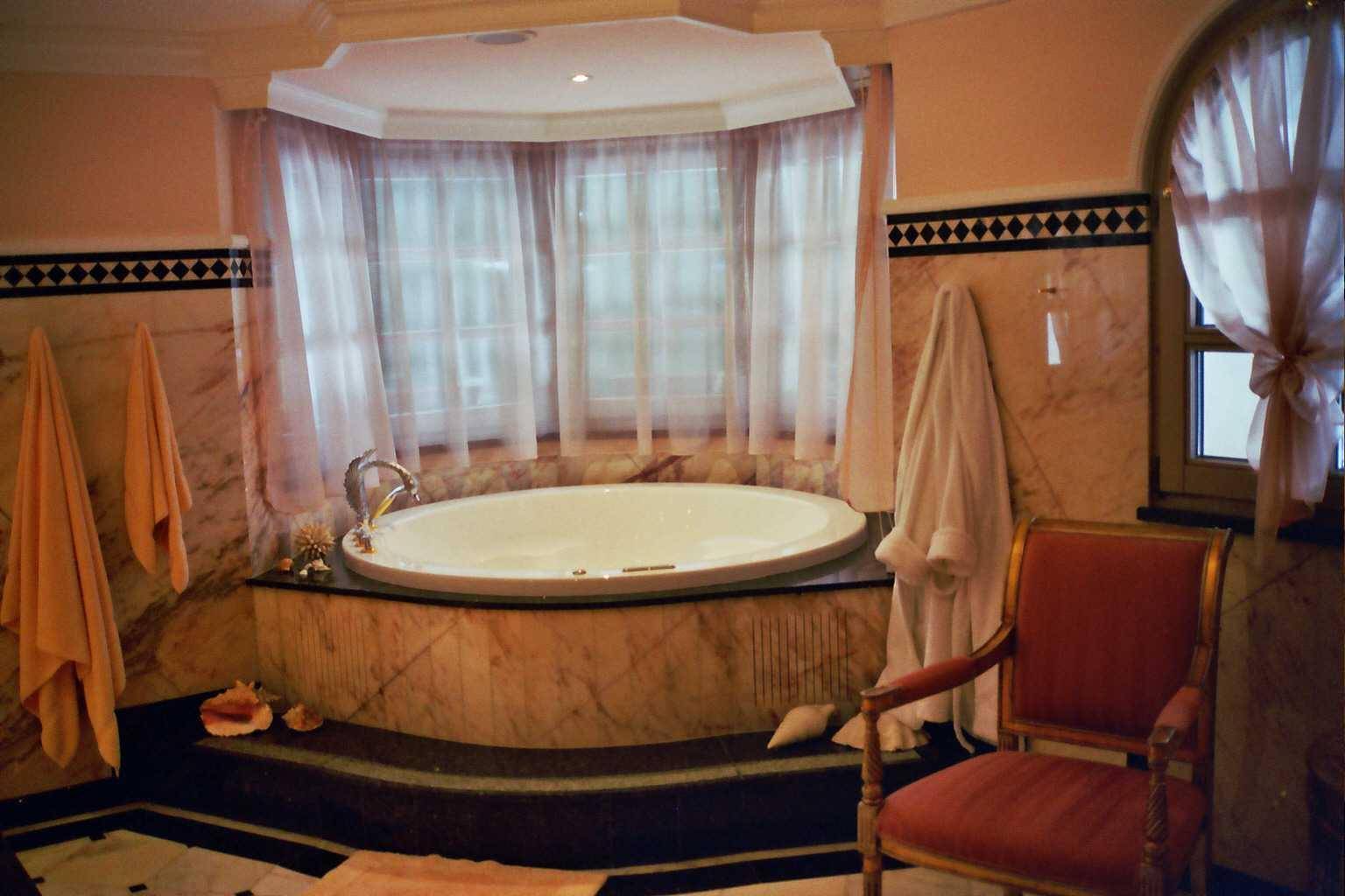 Luxuriöses Badezimmer mit runder Badewanne, Marmorverkleidung und großen Fenstern.