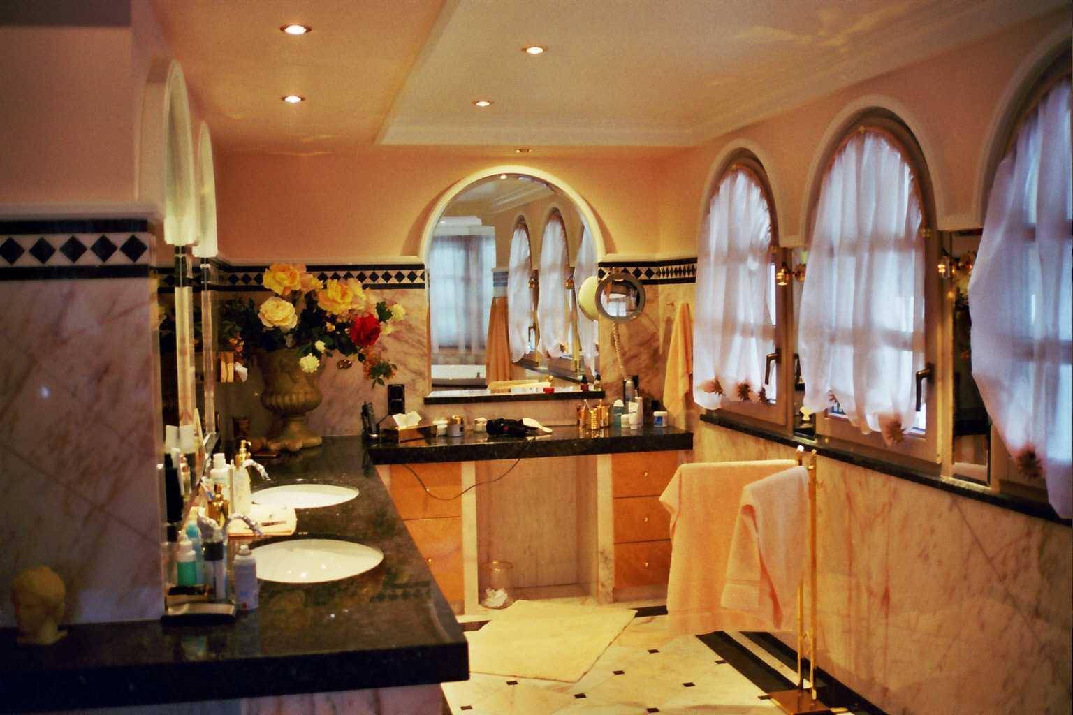 Elegantes Badezimmer mit Doppelwaschbecken, Marmoroberflächen und Rundbogenfenstern.