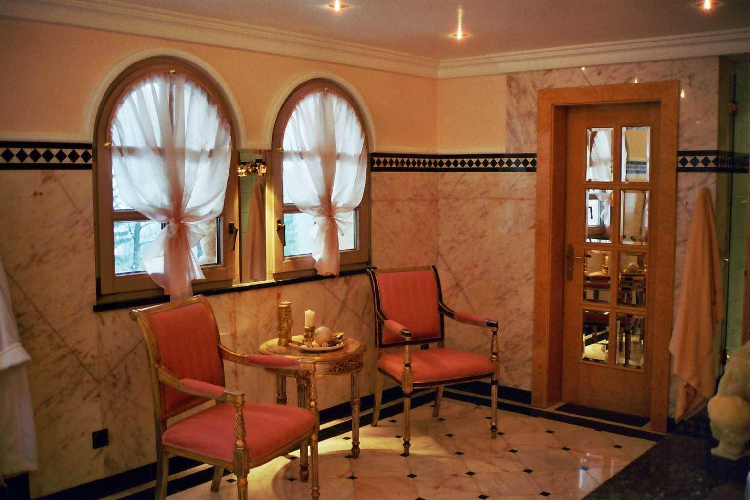 Geräumiges Badezimmer mit Sitzgelegenheiten, Marmorwänden und eleganten Bogenfenstern.