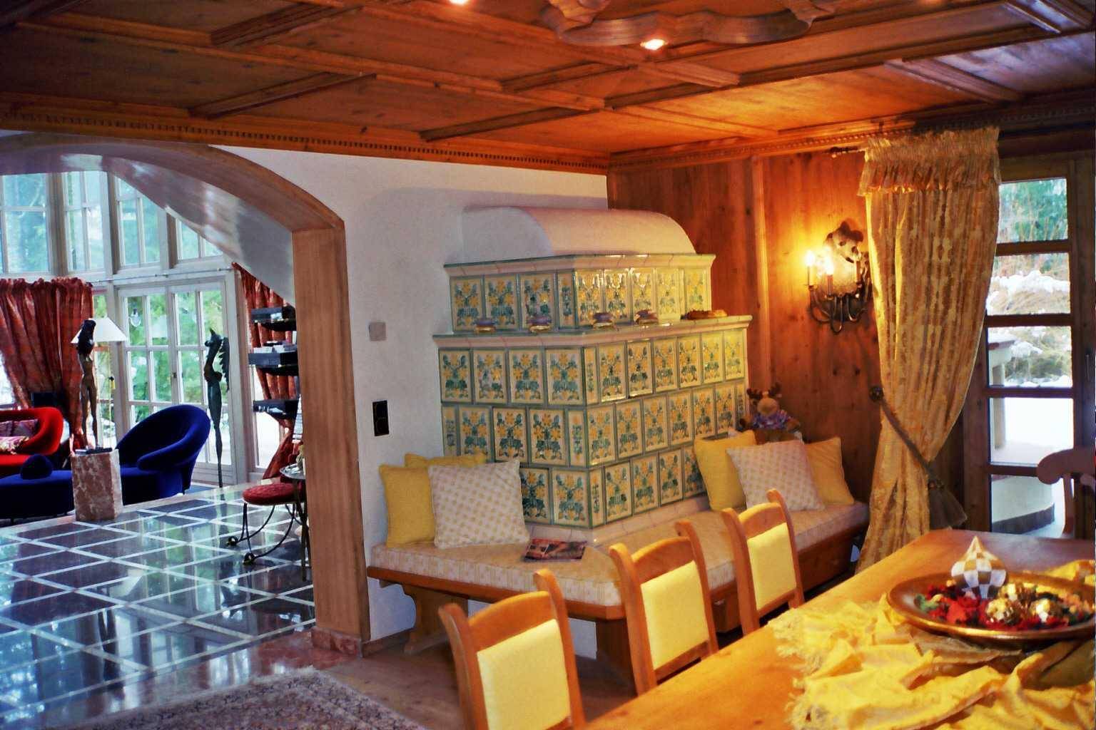 Gemütlicher Essbereich mit traditionellem Kachelofen, Holzbänken und Blick ins Wohnzimmer.